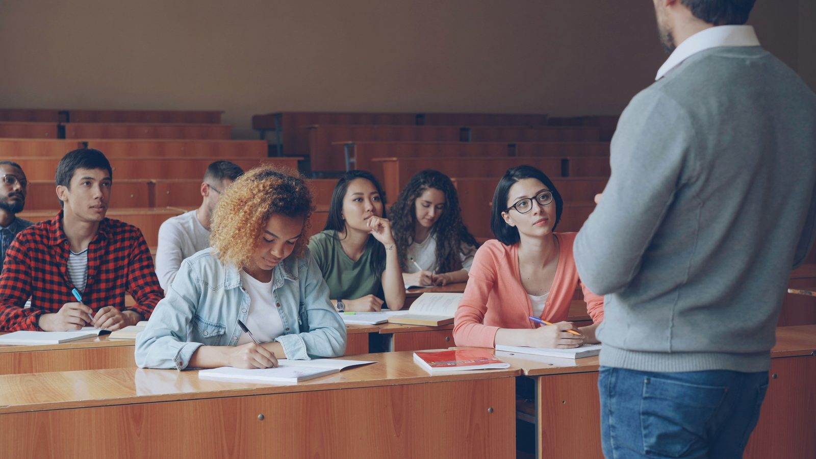 Преподаватель обращается к студентам, конспектирующим в университетской аудитории